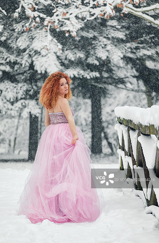 我的冬季童话：身穿华丽粉色连衣裙的美丽女孩在雪林中图片素材