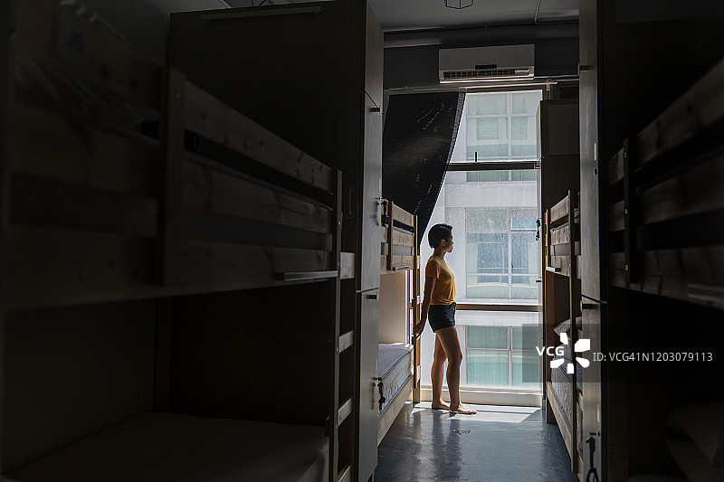 年轻女人凝视着旅馆宿舍房间的窗外图片素材