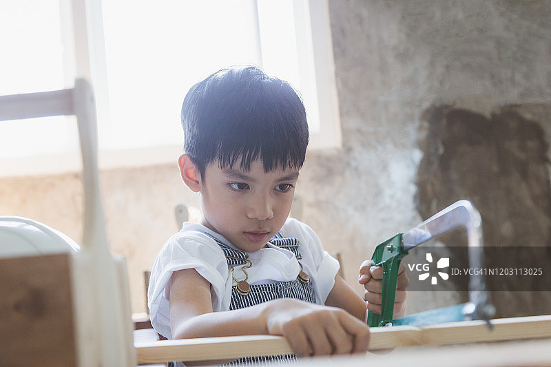 亚洲木匠男孩在木工车间或工作室锯木板图片素材