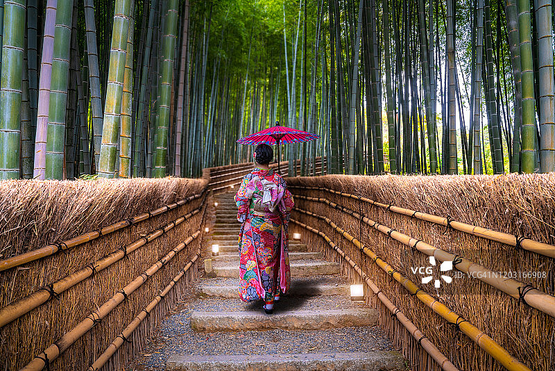 身穿日式传统和服，在京都岚山竹林手持红伞观光的亚洲年轻女游客，日本旅游文化概念图片素材