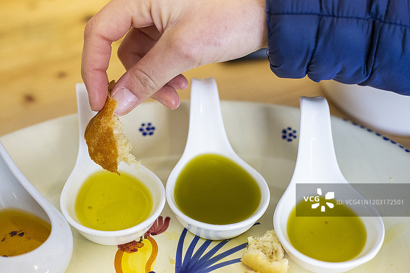 人手将面包蘸入来自意大利普利亚的不同口味的特级初榨橄榄油中图片素材