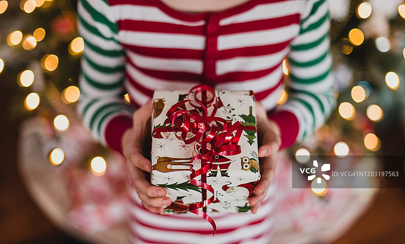 穿着睡衣的孩子在圣诞树灯光前拿着圣诞礼物图片素材