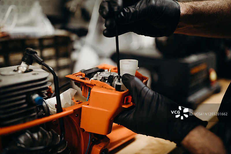 在车间修理链锯化油器的男人图片素材