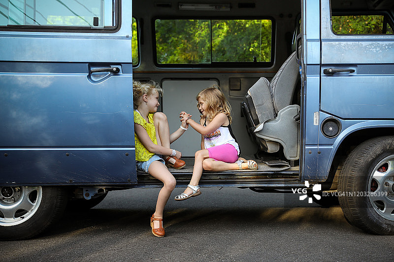 两个女孩坐在老式老爷车的门口手牵着手图片素材