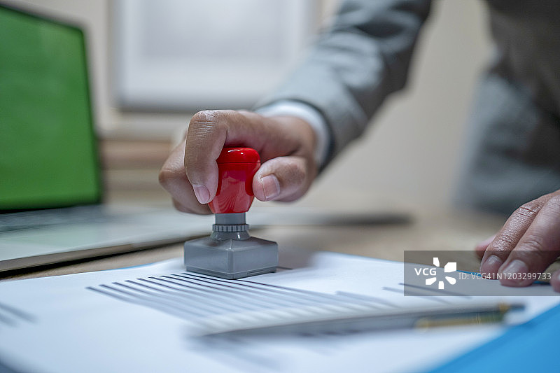 办公桌上手持已批准印章在文件上盖章的人的手部特写图片素材