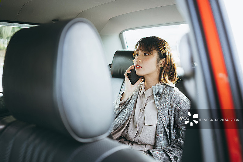 年轻的亚洲女商人坐在出租车的后座上，在城市通勤时匆忙地用智能手机交谈图片素材