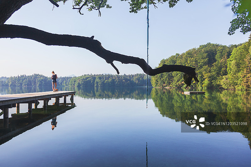 宁静美丽的湖泊，带有码头和跳水台，年轻女子正在欣赏风景图片素材