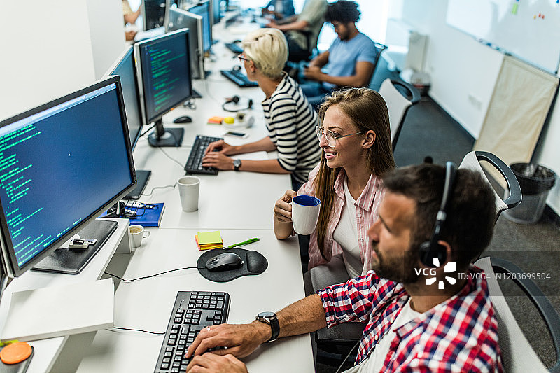 快乐的程序员在办公室里一边喝咖啡一边和同事工作图片素材