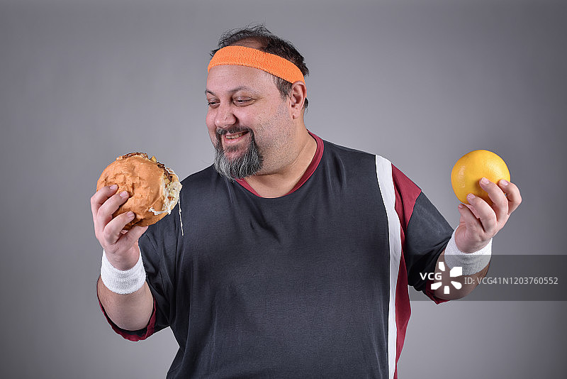 超重男子拿着柑橘和三明治，看起来很高兴图片素材