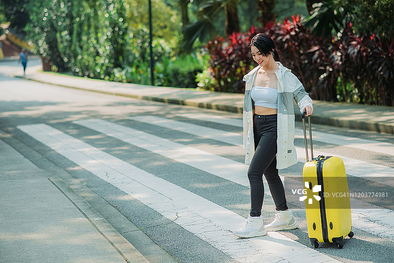 微笑的华人少女拉着行李箱过马路图片素材