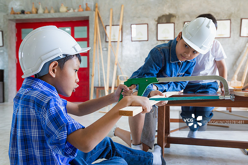 戴着安全帽的亚洲木匠男孩在木工车间锯木板图片素材