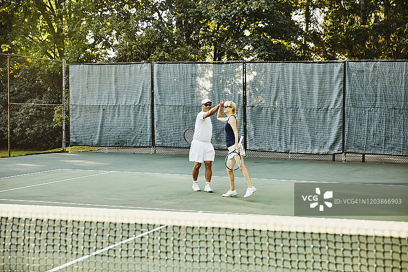 年长的男女网球混双搭档在网球比赛后击掌图片素材