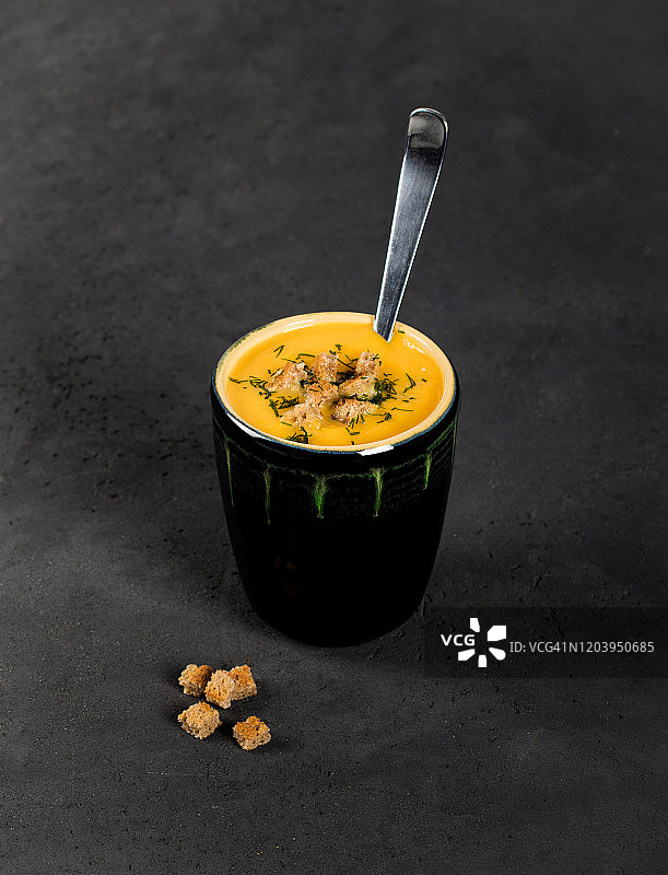 深色背景杯中的奶油烤面包丁南瓜浓汤图片素材