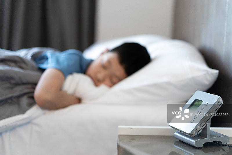 亚洲男孩在床上睡觉，旁边放着闹钟图片素材