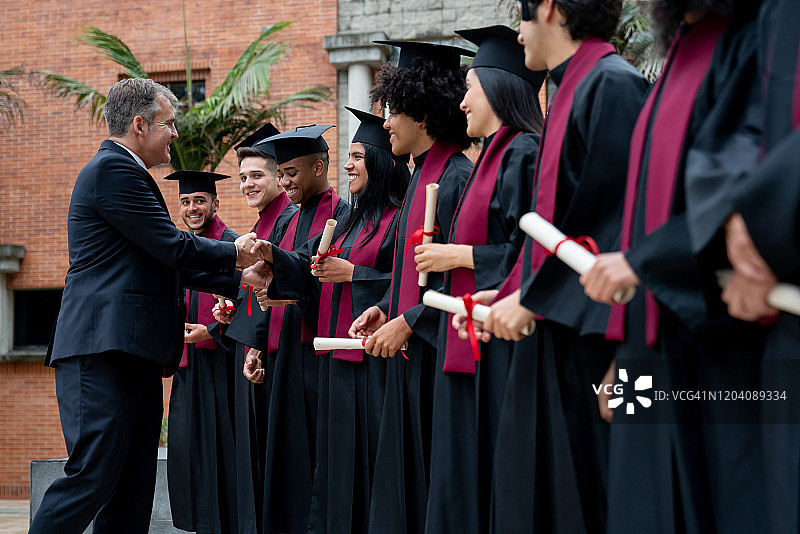 院长在毕业典礼上与一群学生握手图片素材