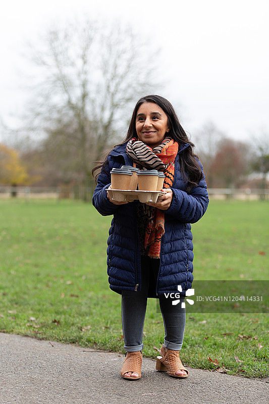 笑容满面的女子手拿一次性咖啡杯站在公园里图片素材