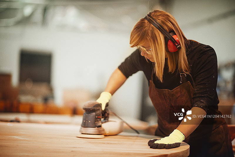 女木工使用随机轨道砂光机打磨木质表面图片素材