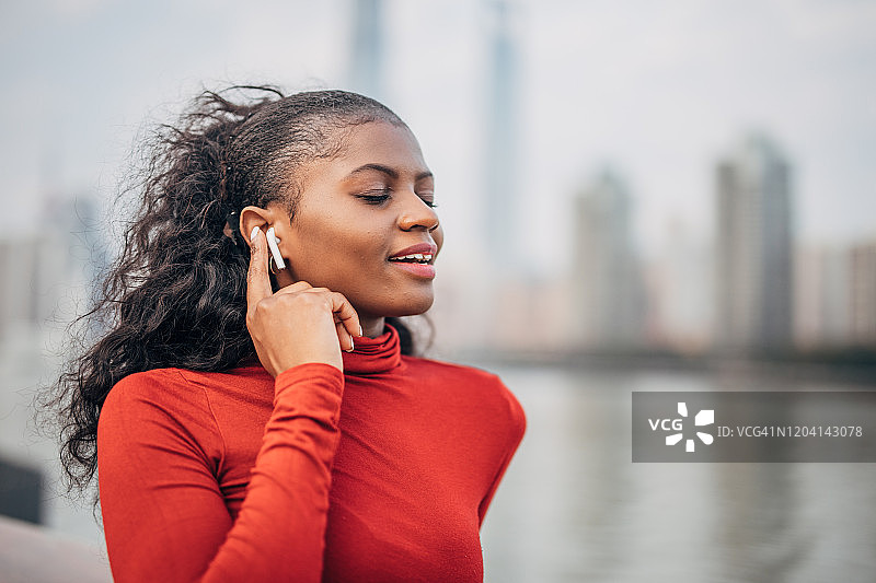 在上海市中心，河边戴着耳机听音乐的黑人女性图片素材
