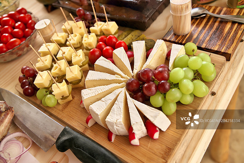 木制砧板上丰盛的奶酪和水果拼盘图片素材