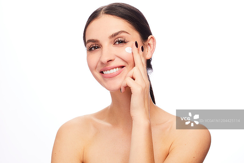 微笑的年轻女人往脸上涂抹乳液图片素材