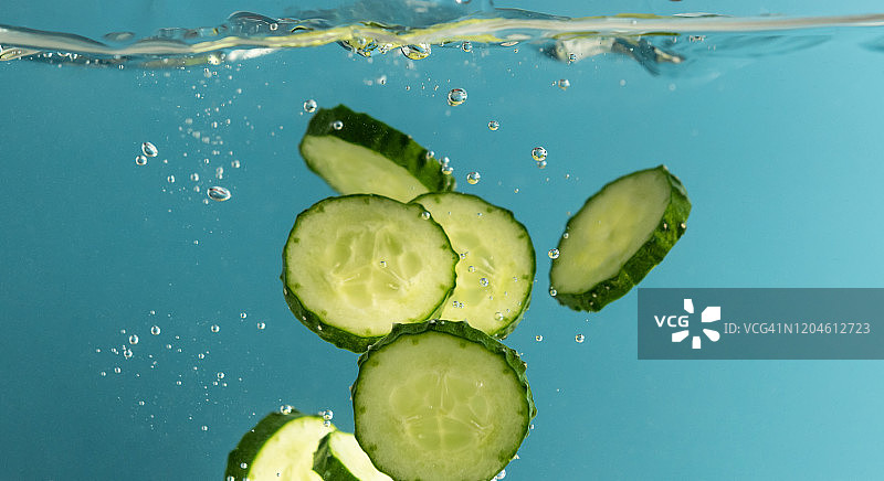 水中飞溅的绿色黄瓜片，蓝色背景图片素材