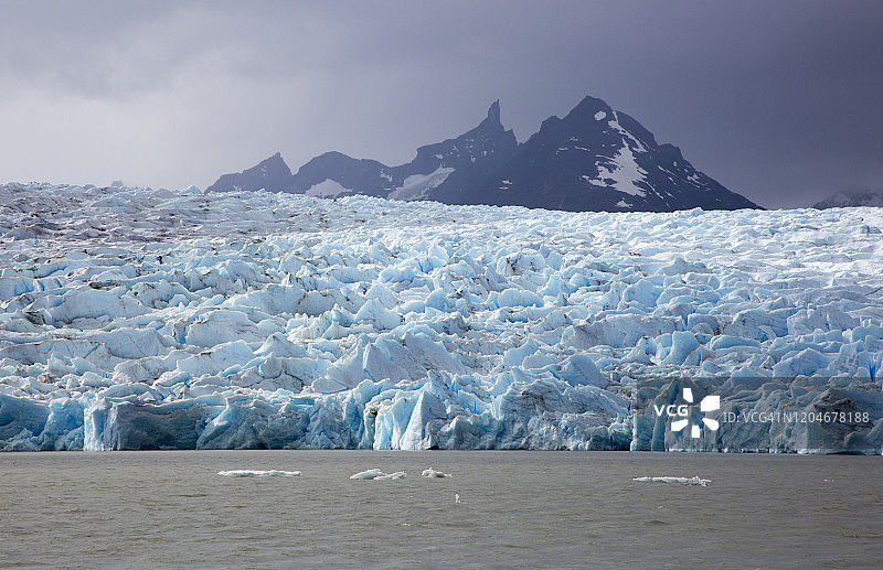 蓝色冰川倾泻入水中，背景是壮观的雪山的长焦镜头照片图片素材