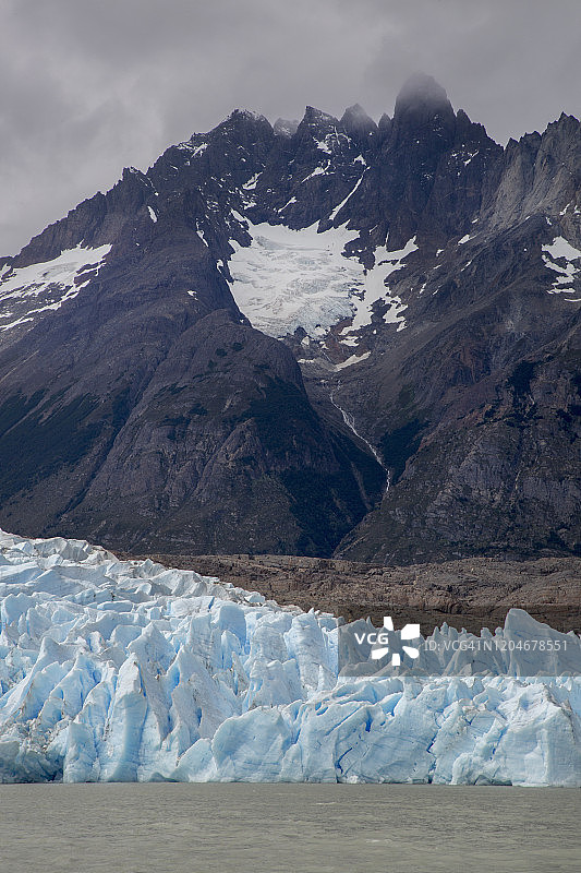 蓝色冰川倾泻入水中，背景是壮观的雪山的长焦镜头照片图片素材