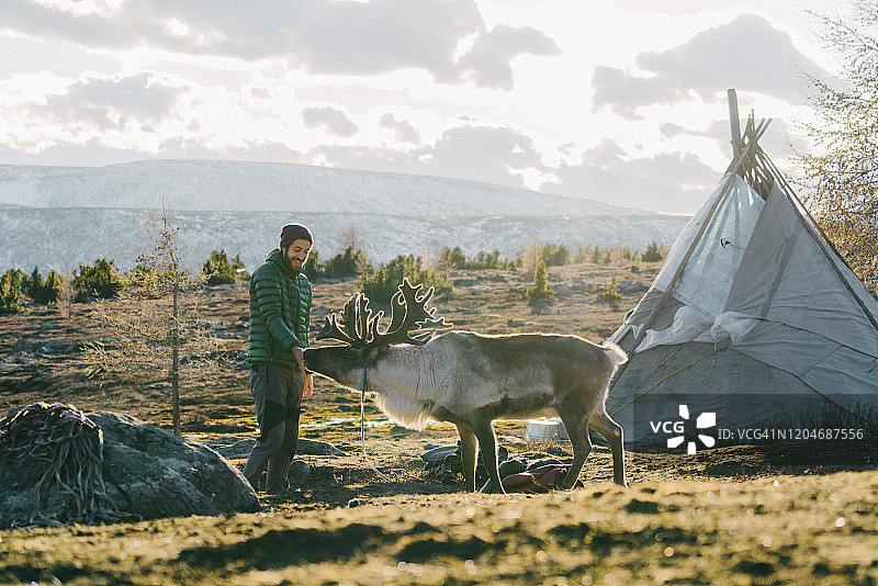 冬天在蒙古的圆锥形帐篷附近站着一头驯鹿的男人图片素材