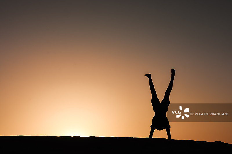 迪拜沙漠日落时分倒立的男孩剪影图片素材