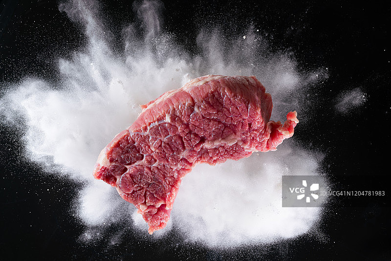 面粉爆炸时牛肉掉入黑色背景图片素材
