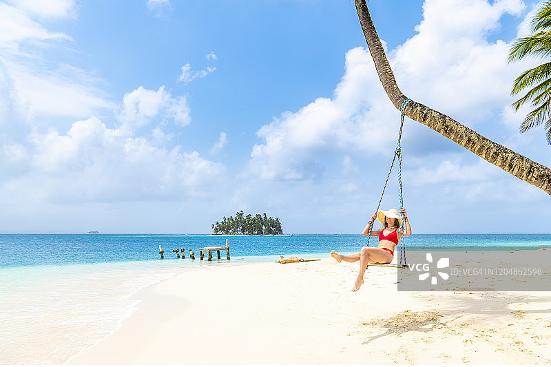 年轻女子在巴拿马圣布拉斯群岛热带海滩的秋千上图片素材