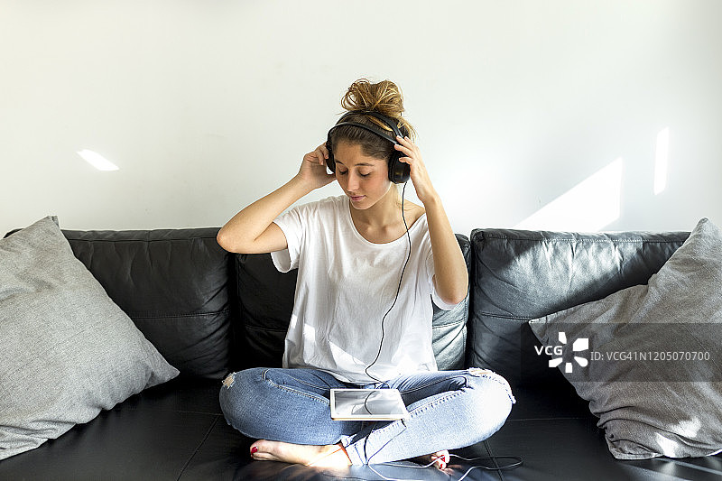 年轻女人坐在沙发上，戴着耳机用平板电脑听音乐图片素材