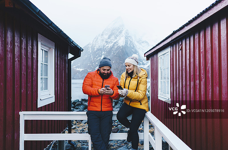 情侣在挪威罗弗敦群岛哈姆诺伊的门廊上使用智能手机图片素材