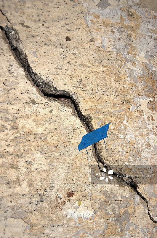 水泥灰泥墙上的裂缝，用蓝色遮蔽胶带和铅笔标记图片素材