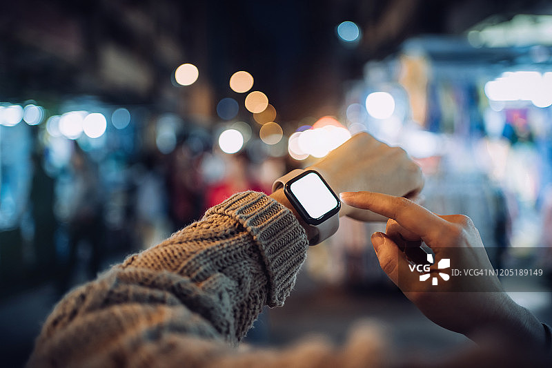 夜晚繁忙的城市街道上，女人使用智能手表的特写镜头图片素材