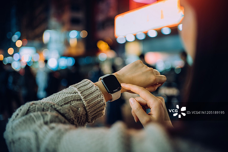 夜晚，年轻女子在熙熙攘攘的城市街道上使用智能手表特写图片素材