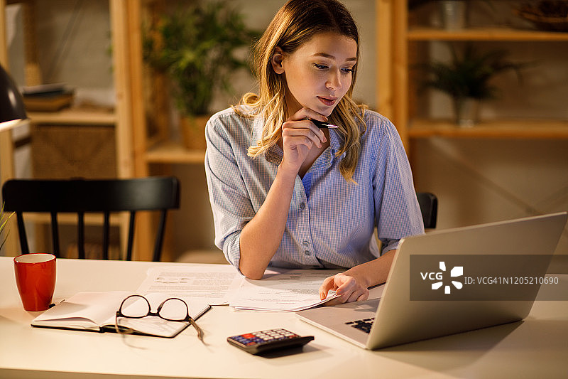 年轻女人在家使用笔记本电脑和计算器工作图片素材