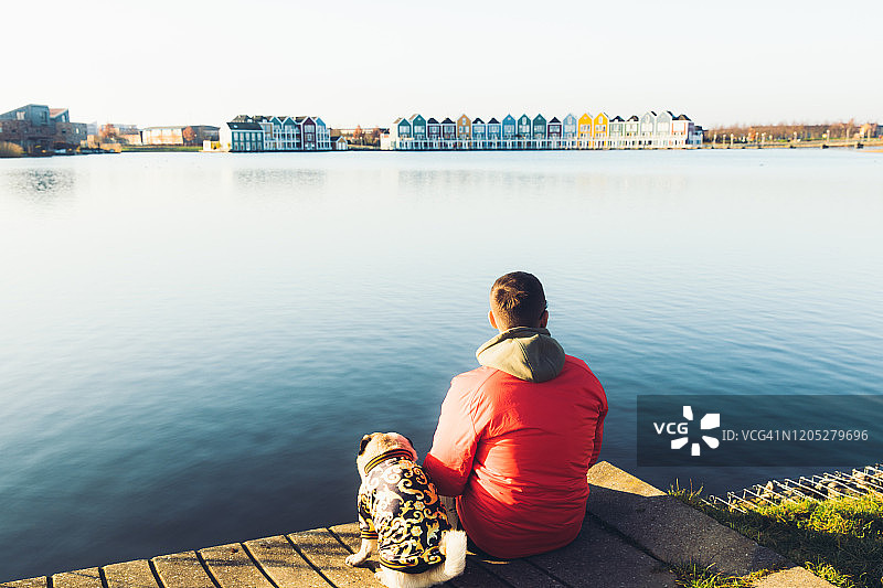 男人和小狗在荷兰的码头上放松身心，欣赏湖边色彩缤纷的建筑图片素材