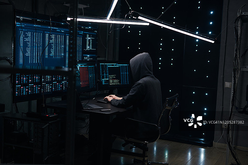 电脑黑客在键盘上编码，背景是显示器和金属架图片素材