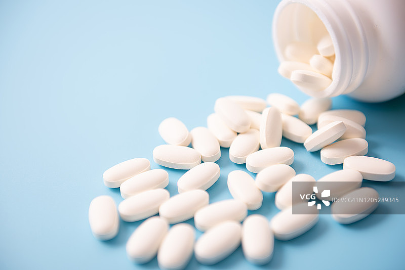 蓝色背景上从瓶子中倒出的钙片图片素材