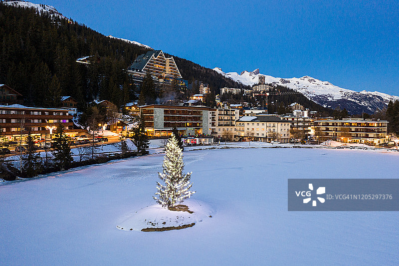 瑞士阿尔卑斯山脉克兰蒙塔纳冰冻湖中央的照明冷杉树图片素材