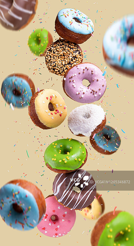在黄色背景上飞舞的彩色甜甜圈，甜蜜美食背景图片素材