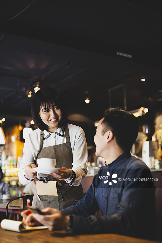 在台北咖啡馆，亚洲女服务员为在桌旁工作的商人提供咖啡图片素材
