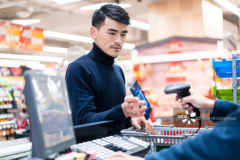 亚洲男子在超市用二维码进行非接触式支付图片素材