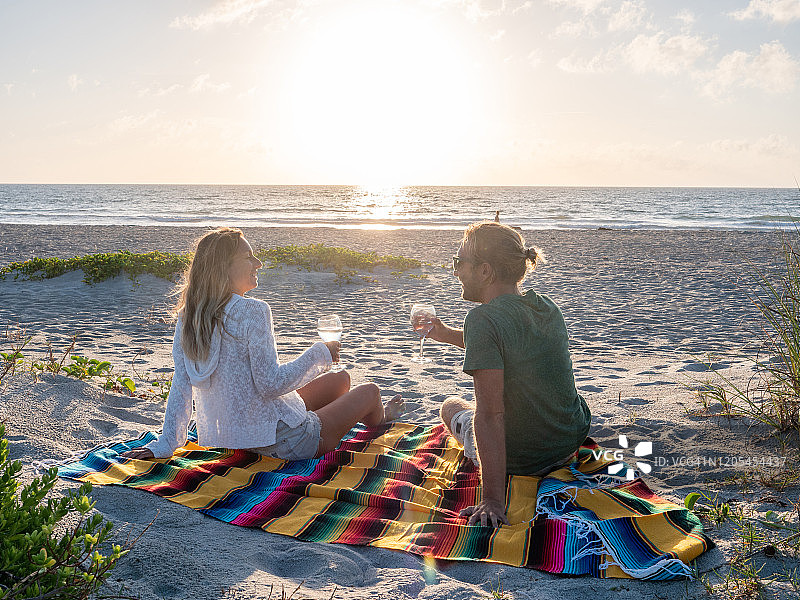 年轻情侣在海滩日落时分享一杯红酒图片素材