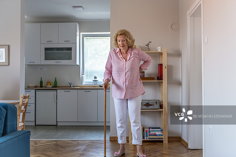 年长的女人术后在家中拄着拐杖进行康复或恢复行走。康复和保健概念图片素材
