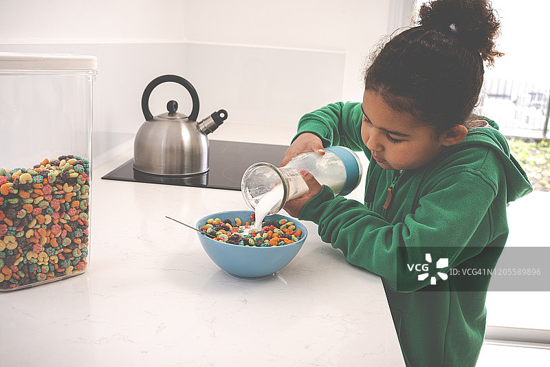 女孩往装有玉米片的蓝色碗里倒牛奶图片素材