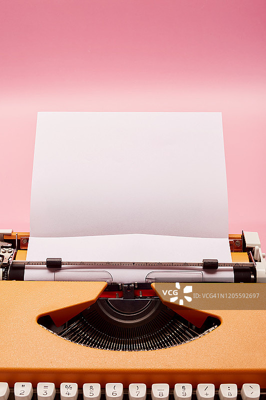 粉色背景上的橙色打字机和空白纸静物图片素材