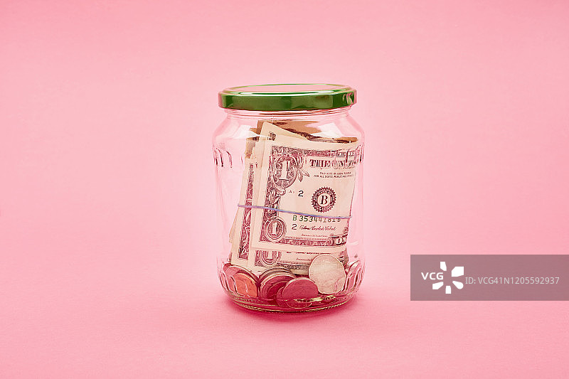 粉色背景下装满美元硬币和纸币的罐子图片素材