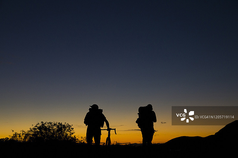 两个背着背包骑自行车的男人走向山上的日落图片素材